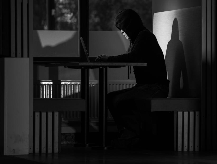 Mann i hettegenser sitter i mørket med laptop